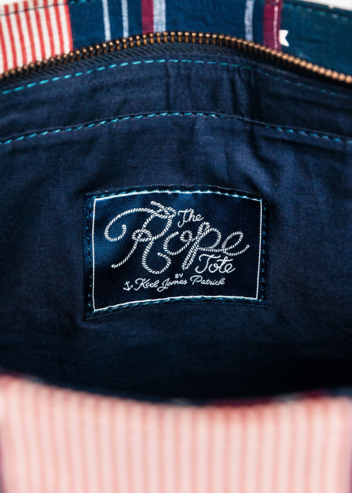 Close-up of a navy blue bag with 'The Rope Tote' label on a striped background.